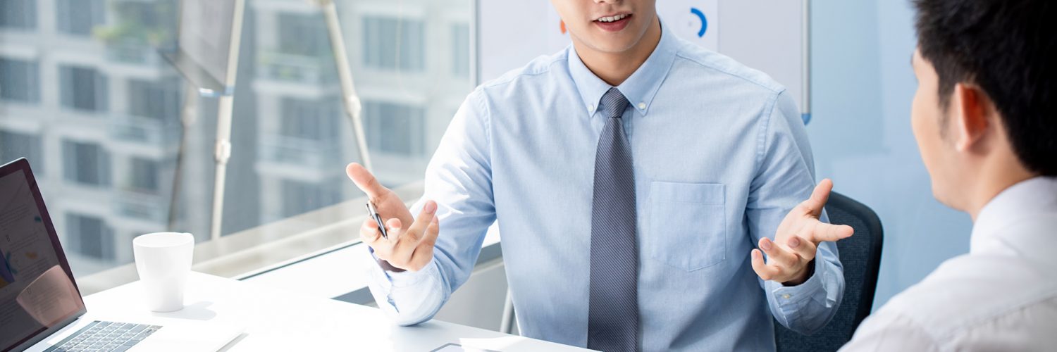 Attractive Asian financial broker explaning business data to his client during their private meeting in the office